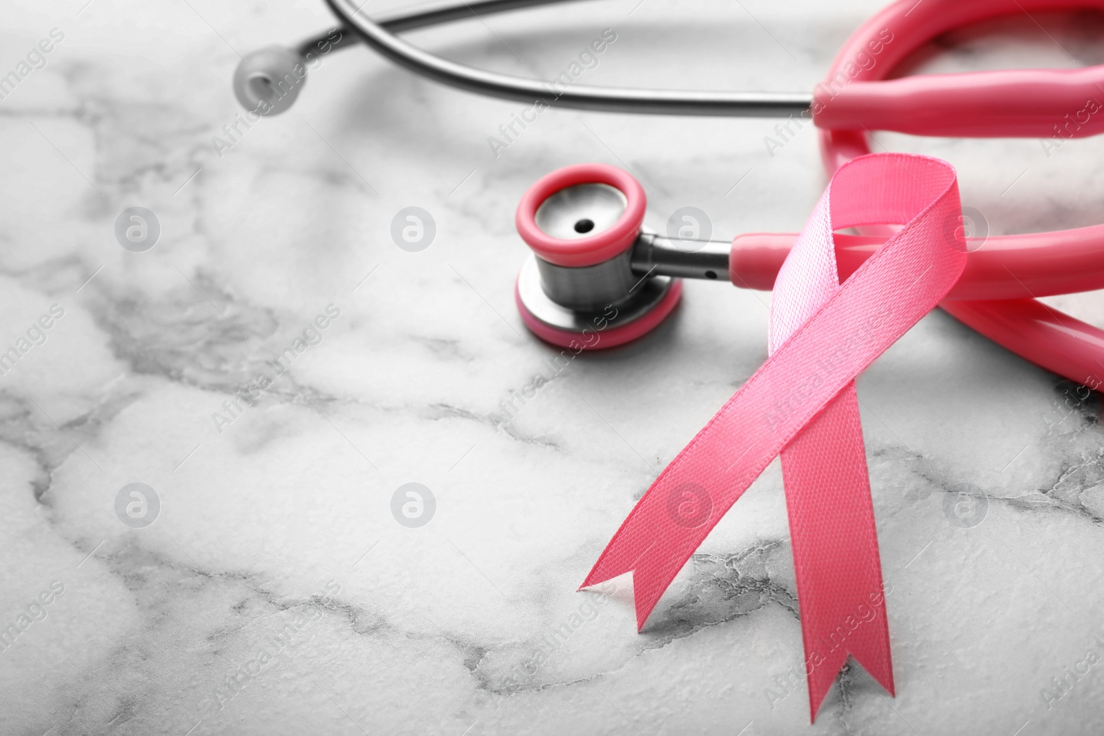 Photo of Pink ribbon and stethoscope on marble background, space for text. Breast cancer concept