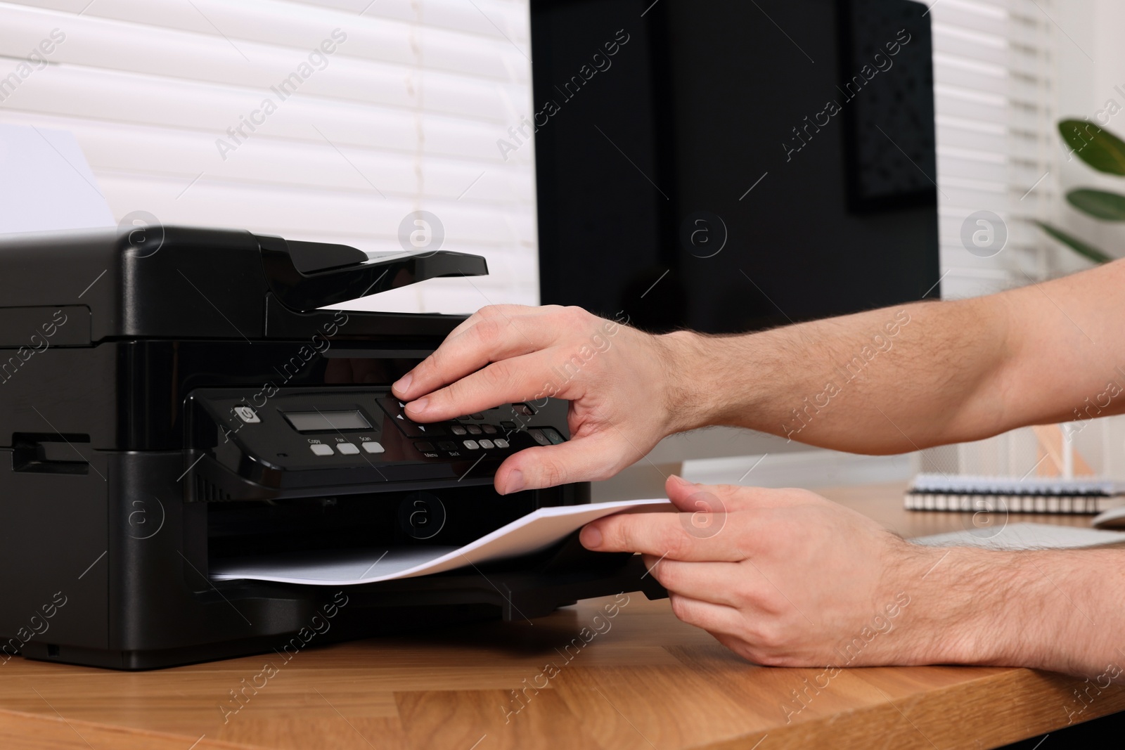 Photo of Man using modern printer at wooden table indoors, closeup