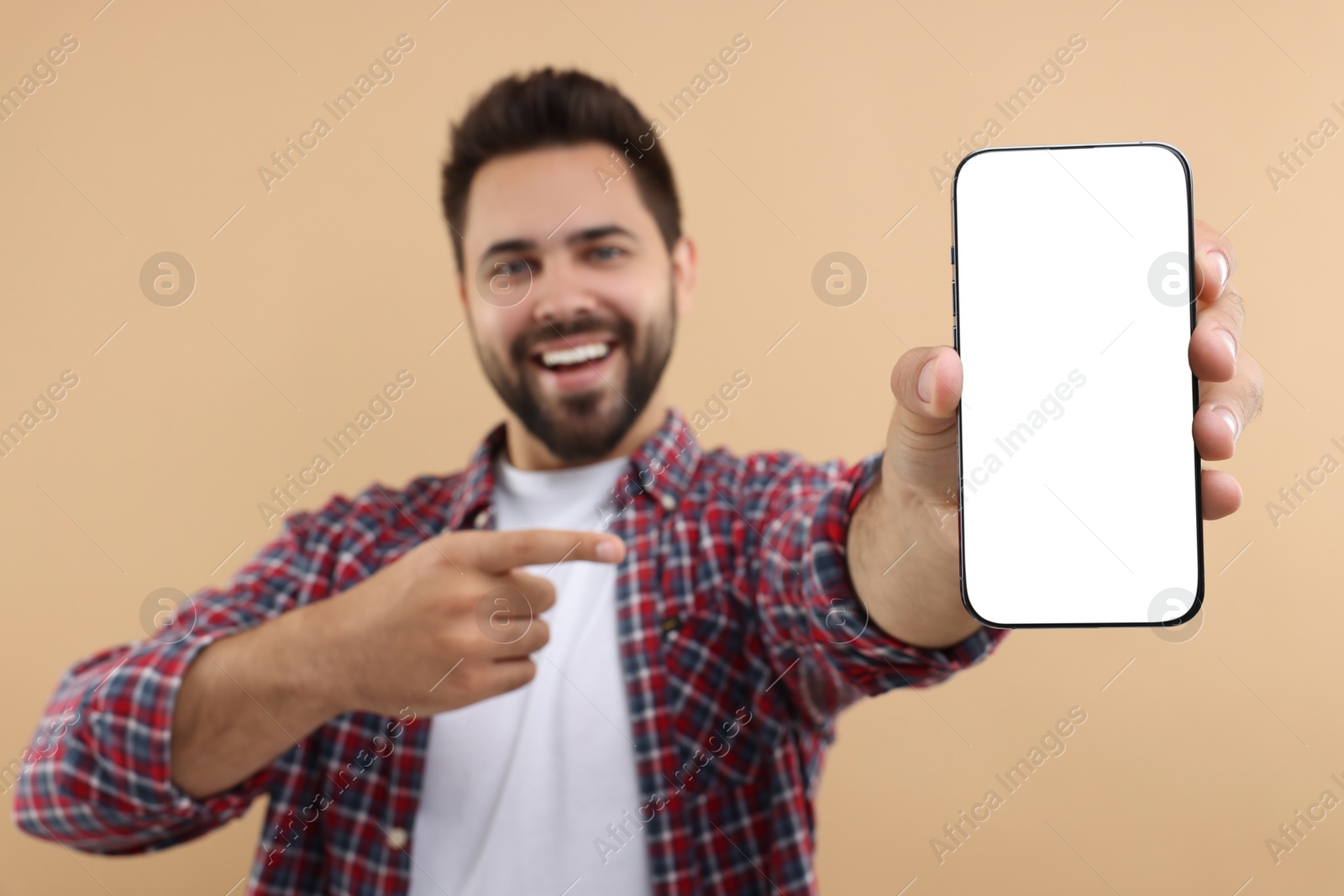 Photo of Young man showing smartphone in hand and pointing at it on beige background, selective focus. Mockup for design