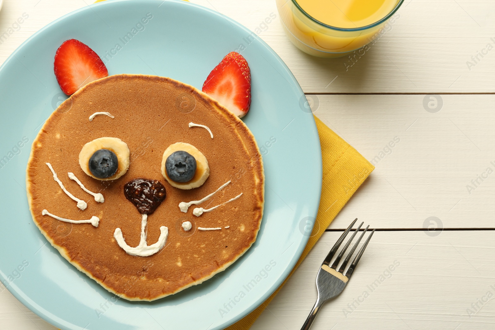 Photo of Creative serving for kids. Plate with cute cat made of pancakes, berries, cream, banana and chocolate paste on white wooden table, top view. Space for text