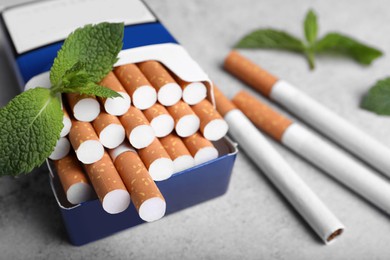 Photo of Pack of menthol cigarettes and mint leaves on grey table, closeup