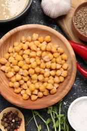 Photo of Delicious chickpeas and different products on black textured table, flat lay. Hummus ingredient