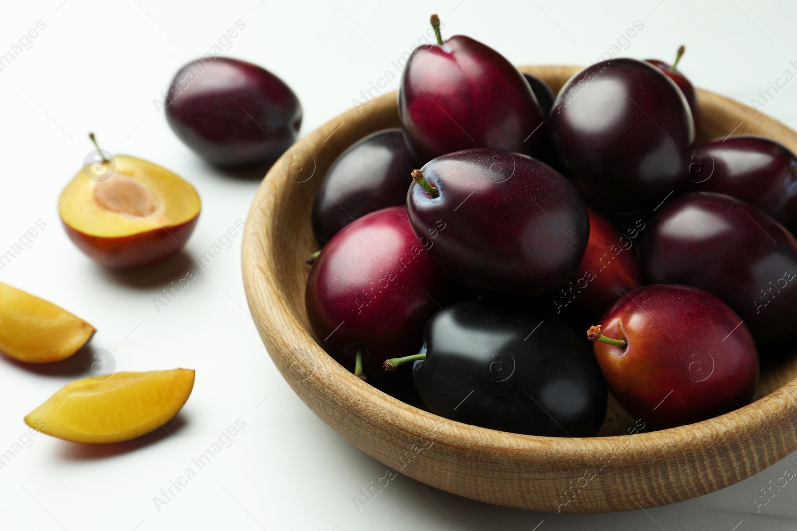 Photo of Bowl with tasty ripe plums on white table, closeup
