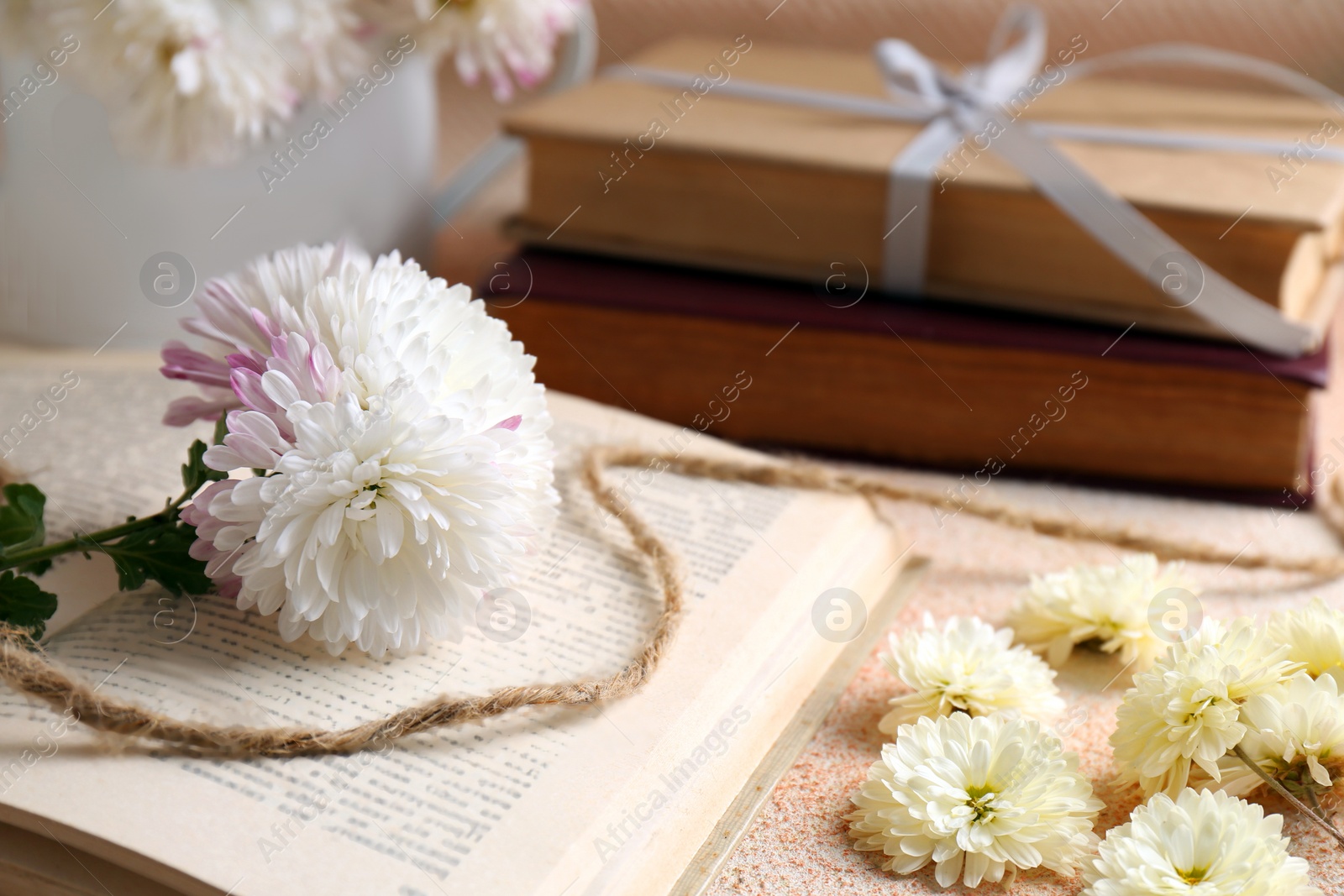 Photo of Book with chrysanthemum flowers as bookmark on beige textured table, closeup. Space for text