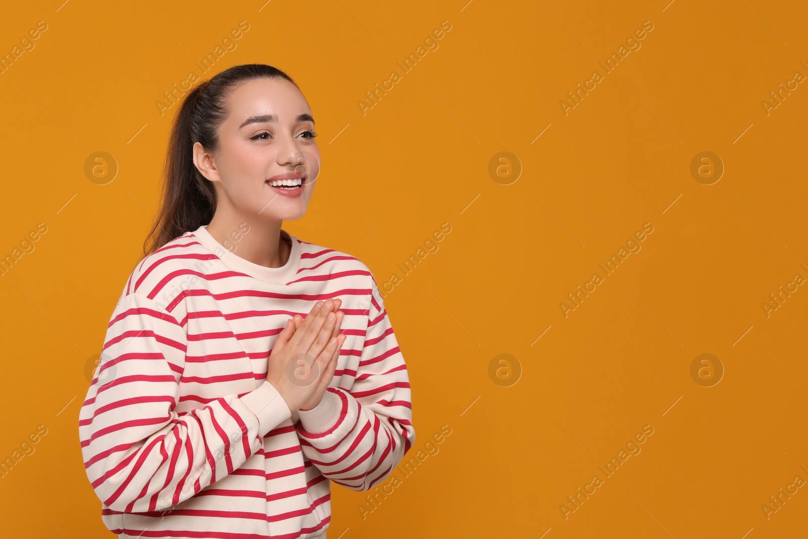 Photo of Thank you gesture. Beautiful grateful woman with hands clasped together on orange background, space for text