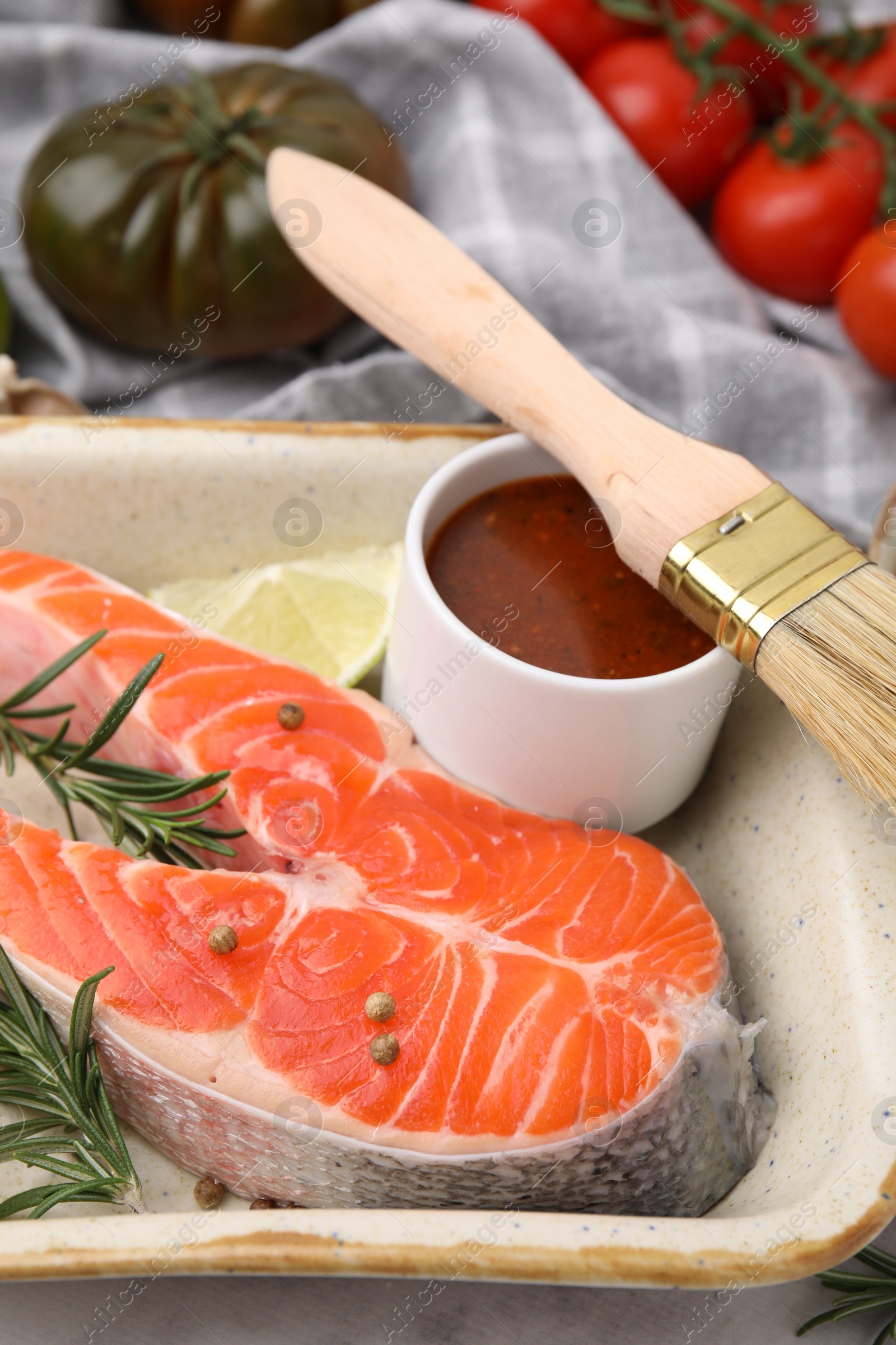 Photo of Fresh fish, lime, rosemary and marinade in baking dish on table, closeup