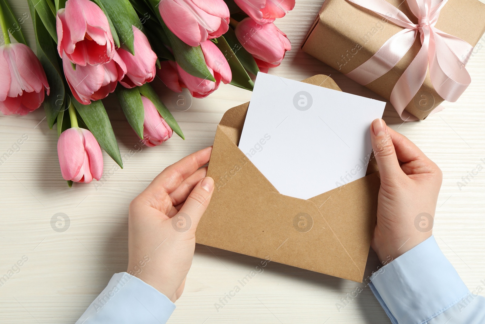 Photo of Happy Mother's Day. Woman holding envelope with blank card at white wooden table, top view