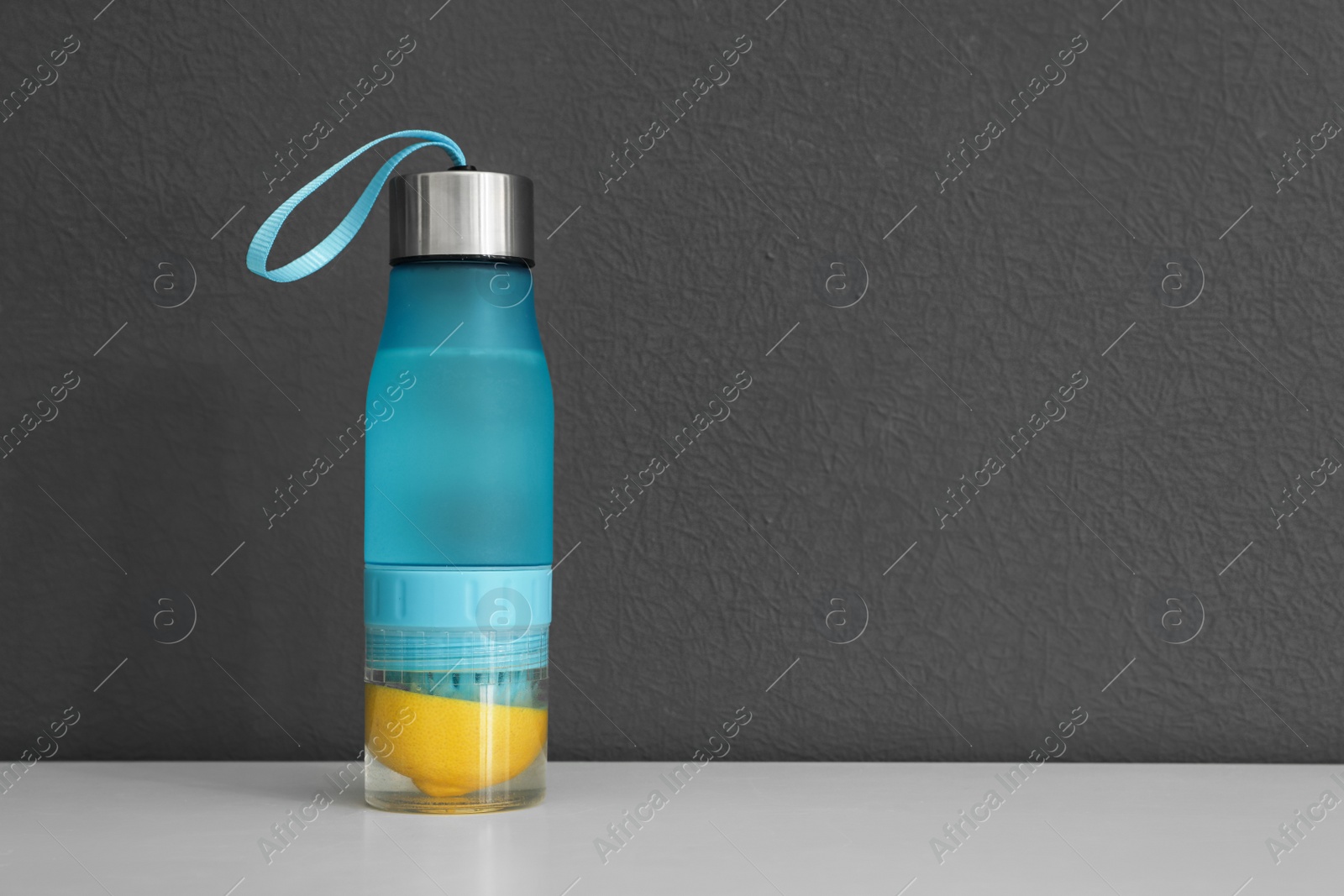 Photo of Sport bottle with lemon water on gray background. Space for text