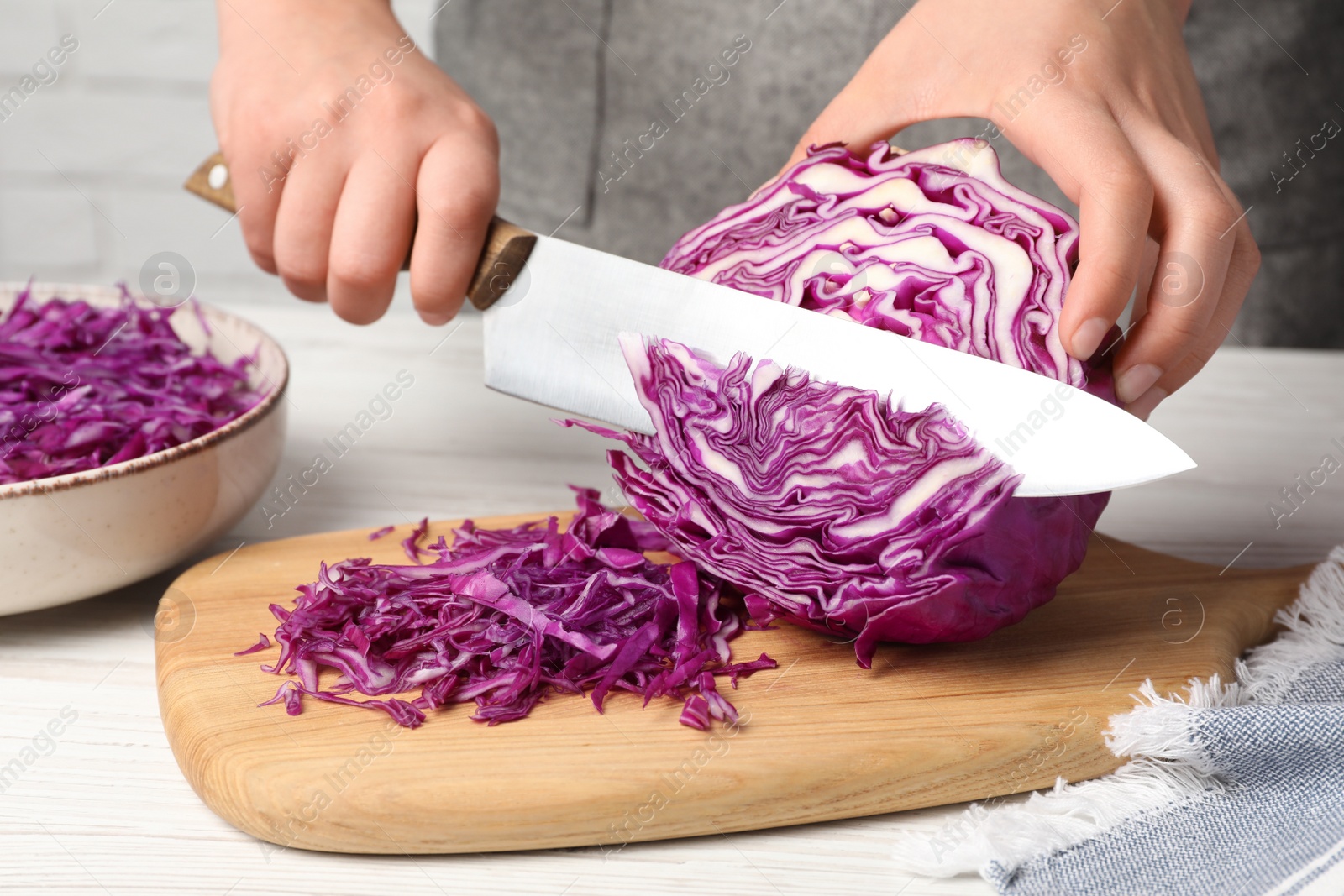 Photo of Woman cutting fresh red cabbage at white wooden table, closeup