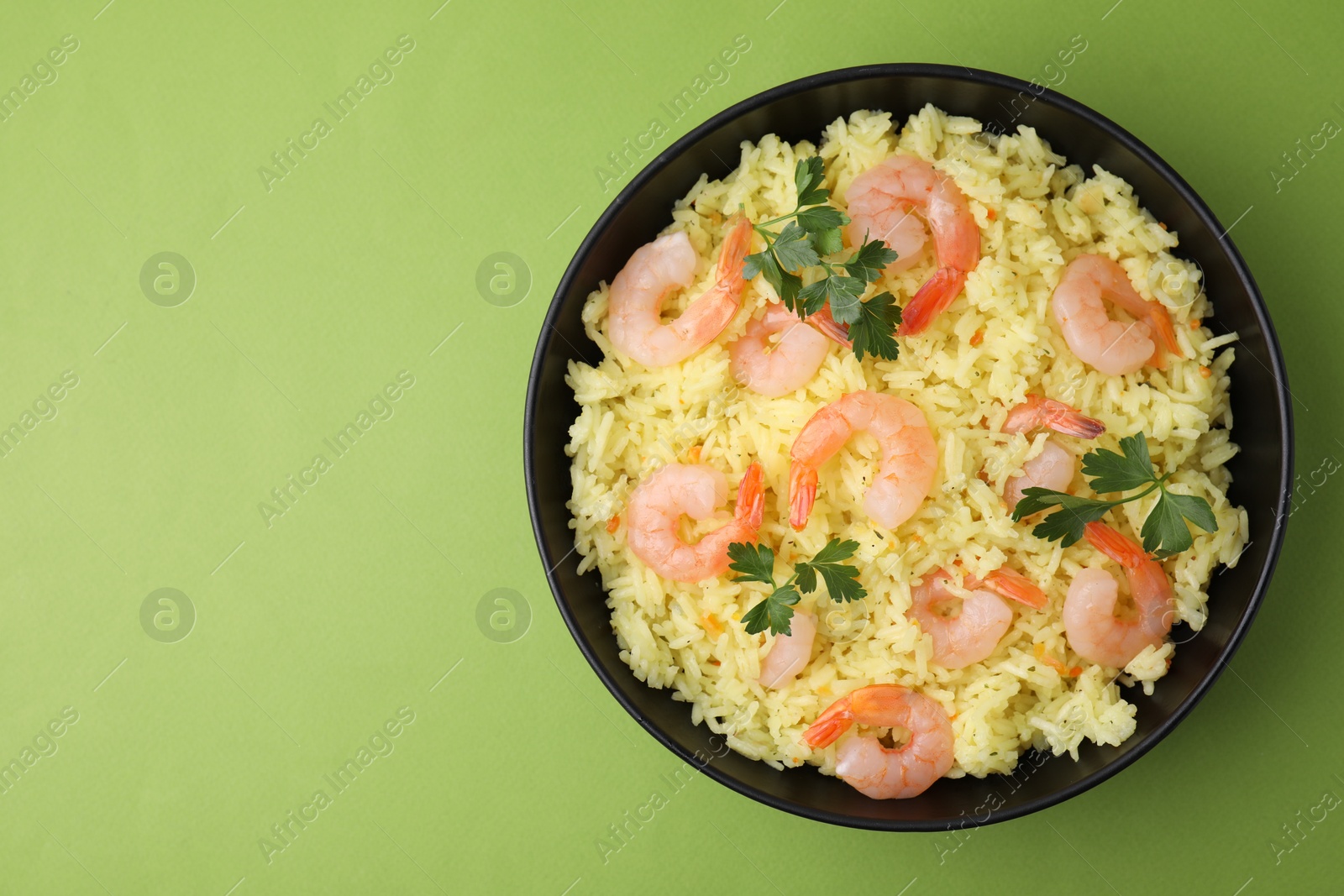 Photo of Delicious risotto with shrimps and parsley in bowl on light green background, top view. Space for text