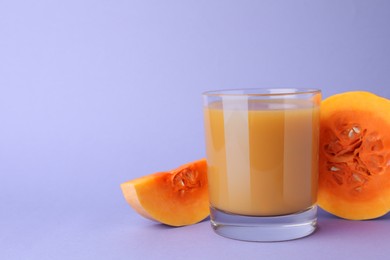 Tasty pumpkin juice in glass and cut pumpkin on lavender color background. Space for text