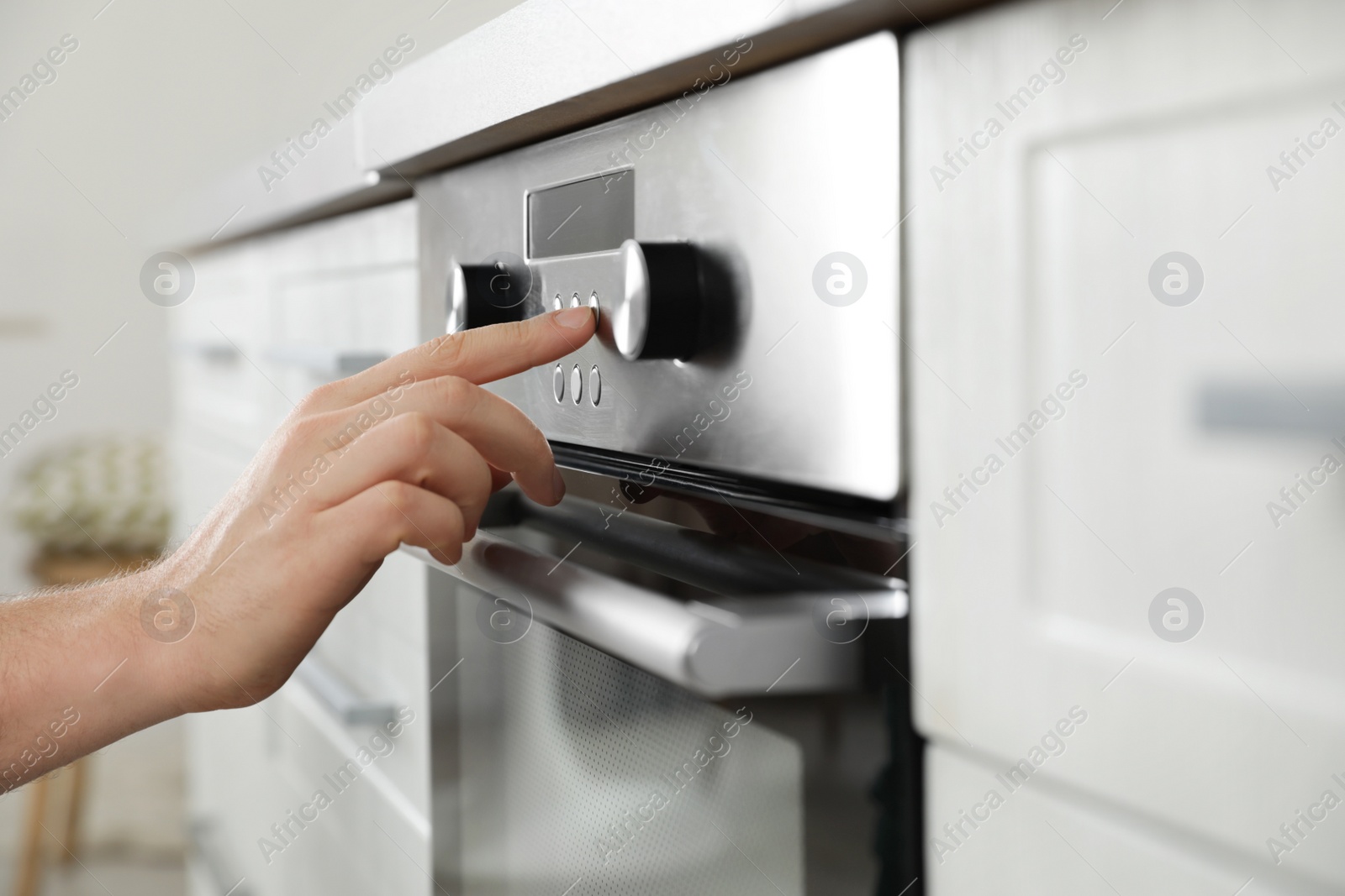 Photo of Man regulating cooking mode on oven panel in kitchen, closeup