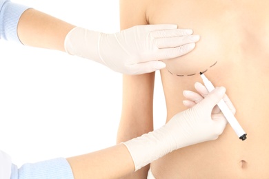 Photo of Doctor drawing marks on patient's breast for cosmetic surgery operation against white background, closeup