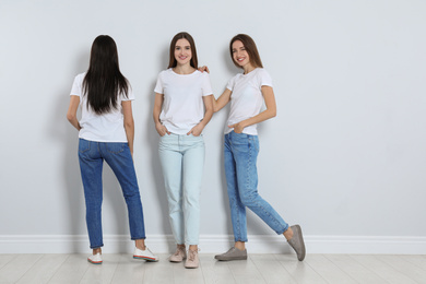 Photo of Group of young women in stylish jeans near light wall