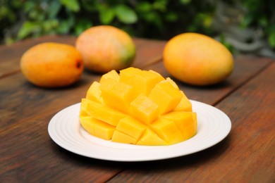 Photo of Delicious ripe cut and whole mangos on wooden table outdoors