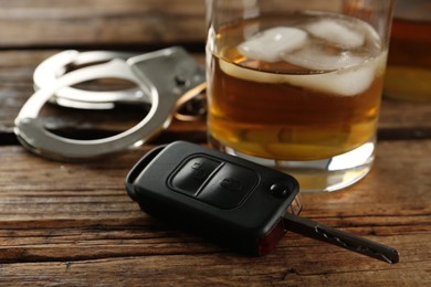 Photo of Glass of alcohol, handcuffs near car key on wooden table, closeup. Dangerous drinking and driving