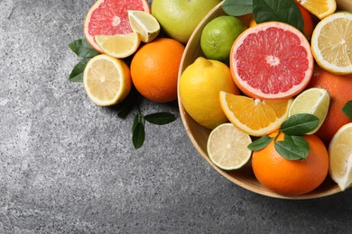 Different fresh citrus fruits and leaves in bowl on grey textured table, flat lay. Space for text