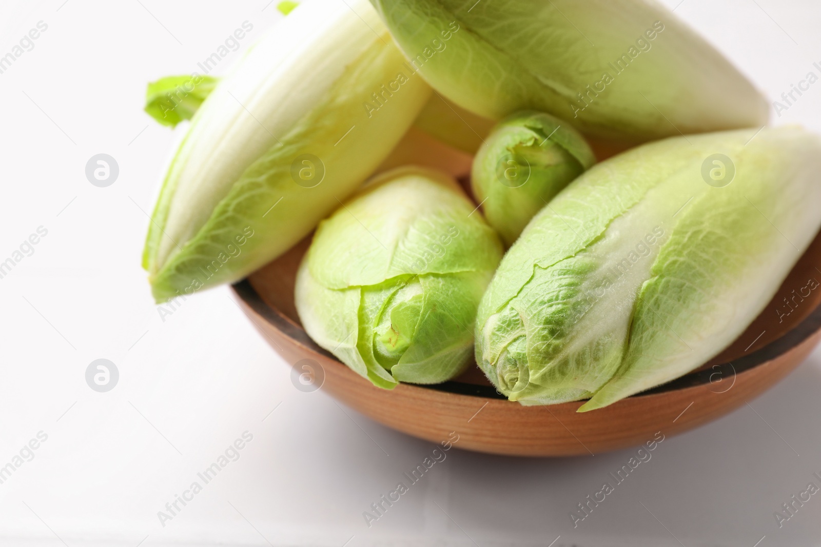 Photo of Fresh raw Belgian endives (chicory) in bowl on white tiled table, closeup