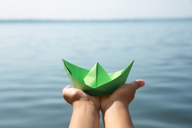 Photo of Child holding green paper boat near river, closeup