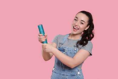 Photo of Young woman blowing up party popper on pink background, space for text