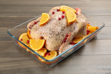 Raw chicken with orange slices and cranberries on wooden table
