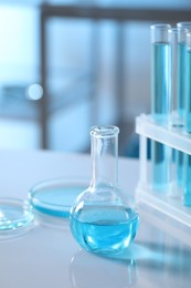 Different glassware and test tubes with light blue liquid on table in laboratory