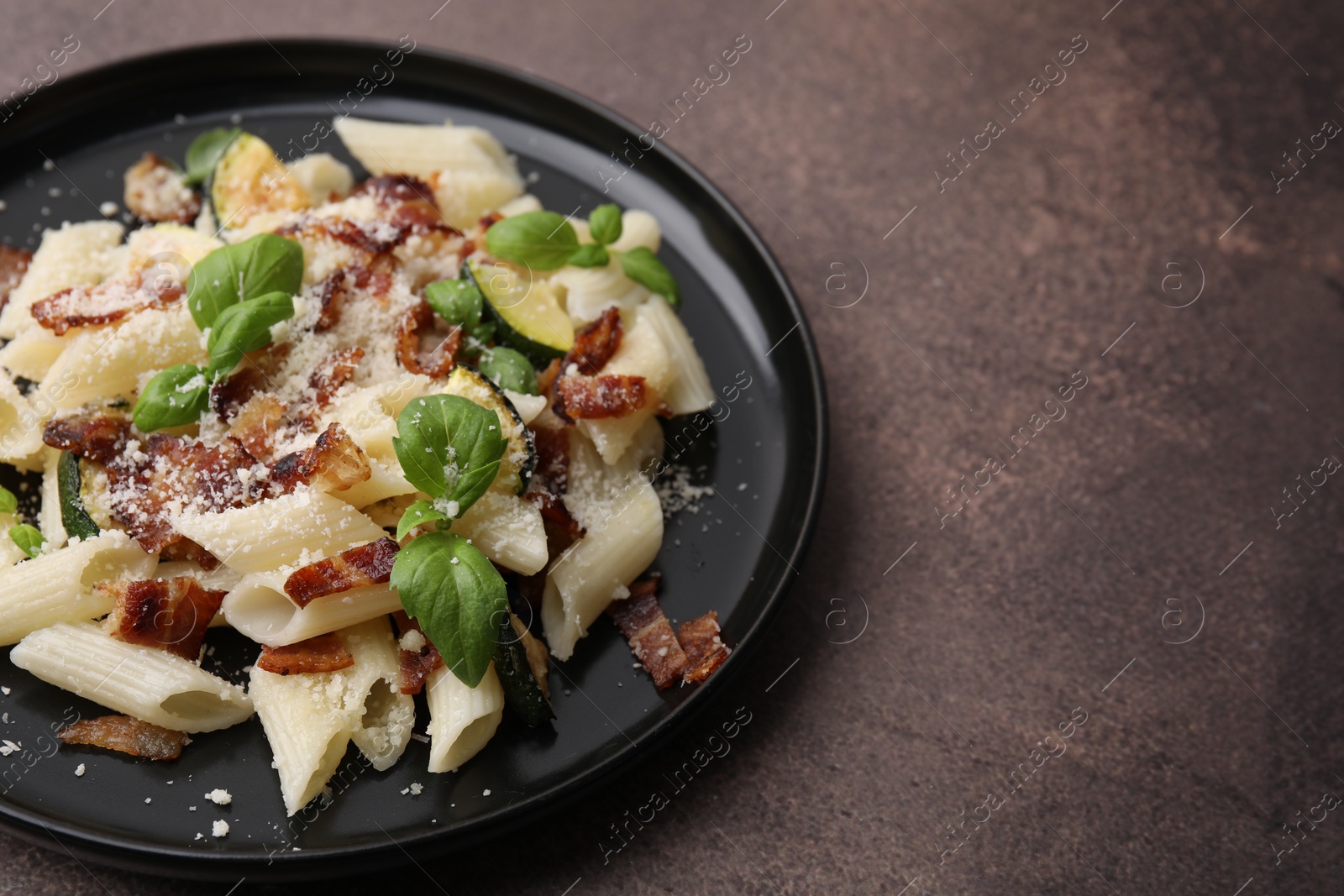 Photo of Tasty pasta with bacon and basil on brown table, space for text