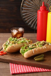 Photo of Tasty hot dogs with chili, lettuce, pickles and sauces on wooden table