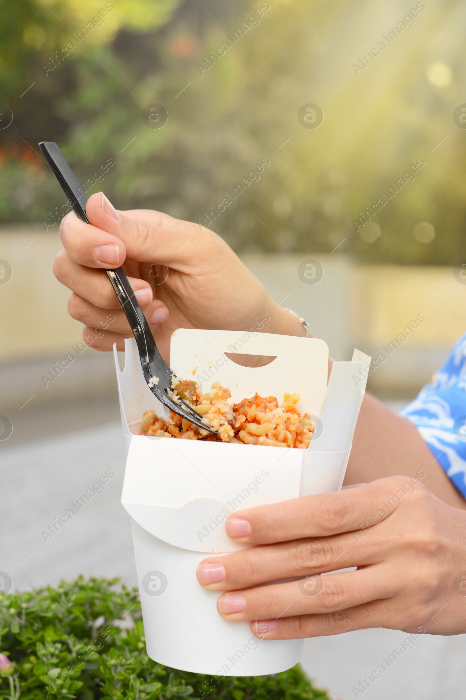 Photo of Woman eating takeaway noodles from paper box with fork outdoors, closeup. Street food