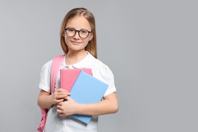 Photo of Cute girl in glasses with backpack and books on light grey background. Space for text