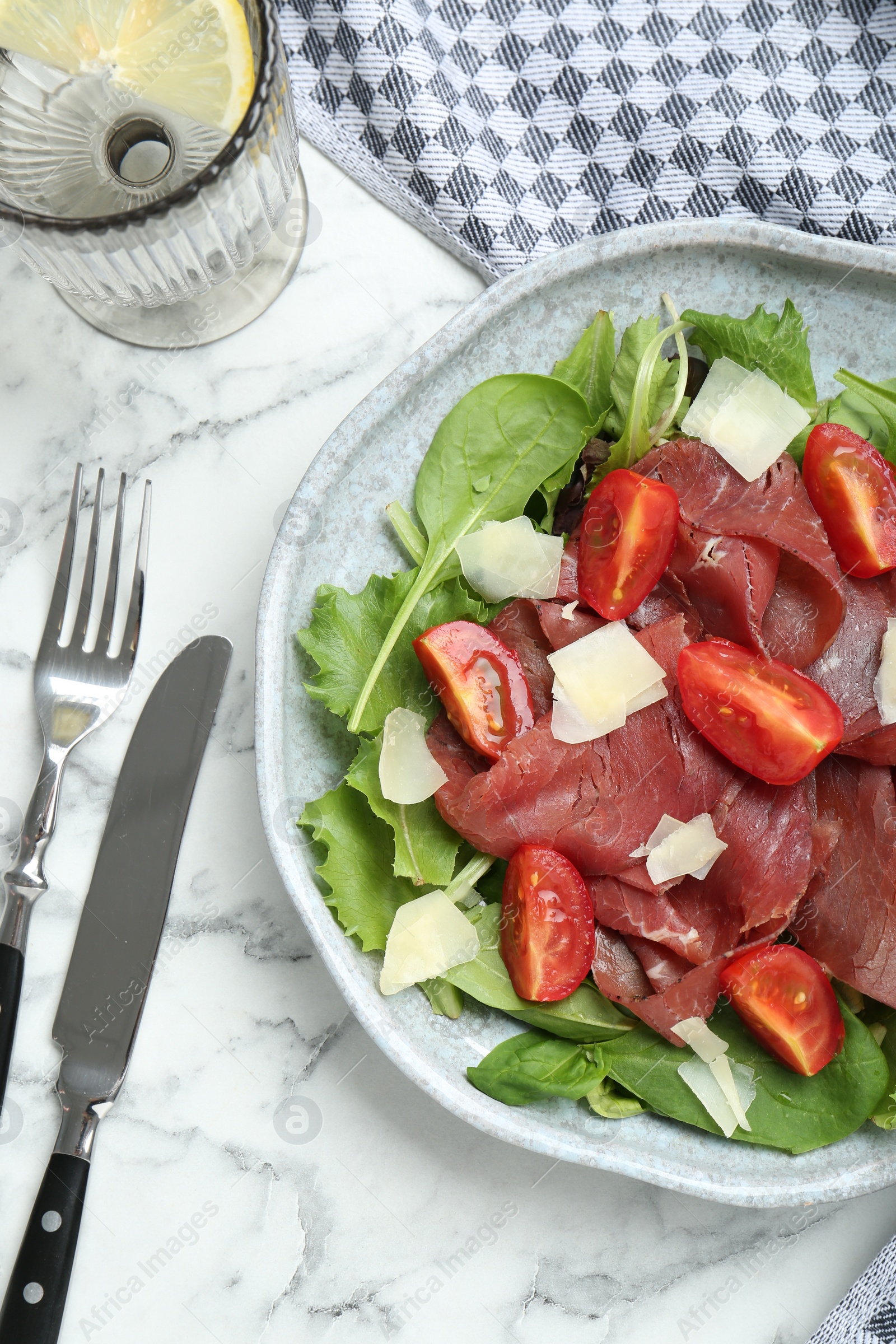 Photo of Delicious bresaola salad with tomatoes and parmesan cheese served on white marble table, flat lay