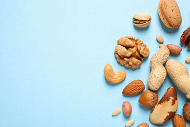 Different delicious nuts on light blue background, flat lay. Space for text