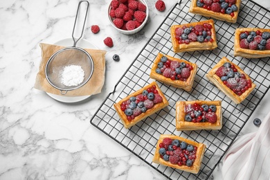 Cooling rack and fresh delicious puff pastry with sweet berries on white marble table, flat lay