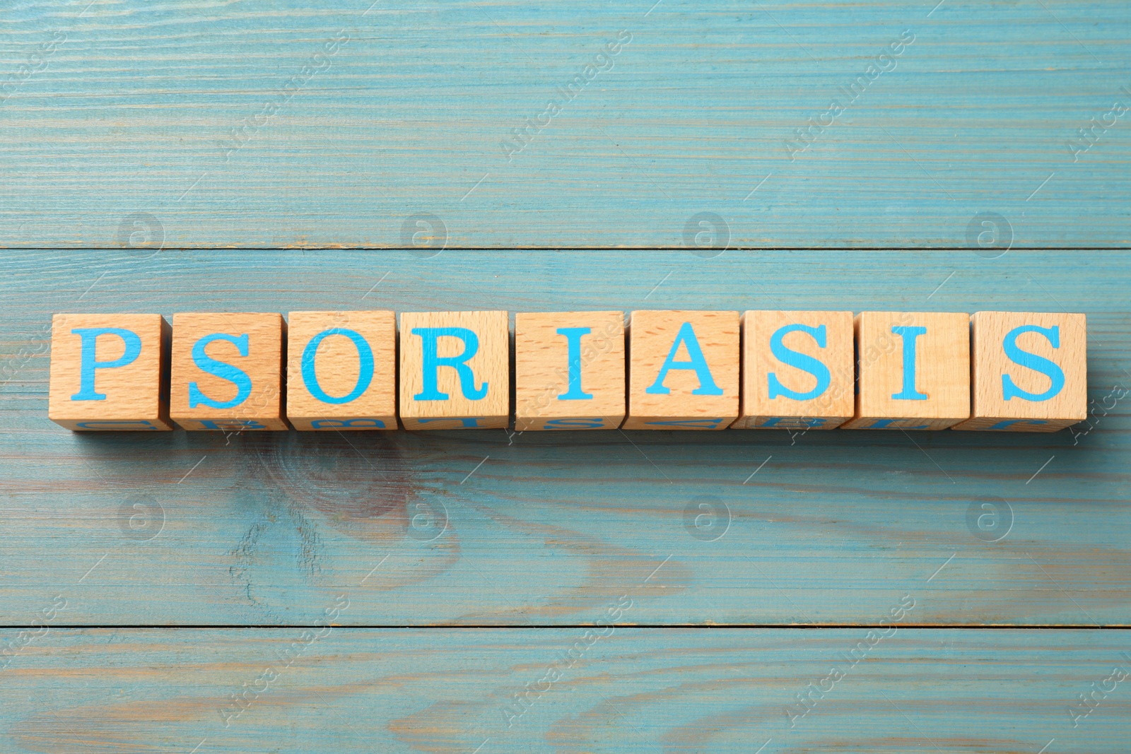 Photo of Word Psoriasis made of cubes with letters on blue light wooden table, top view