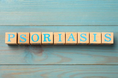 Photo of Word Psoriasis made of cubes with letters on blue light wooden table, top view