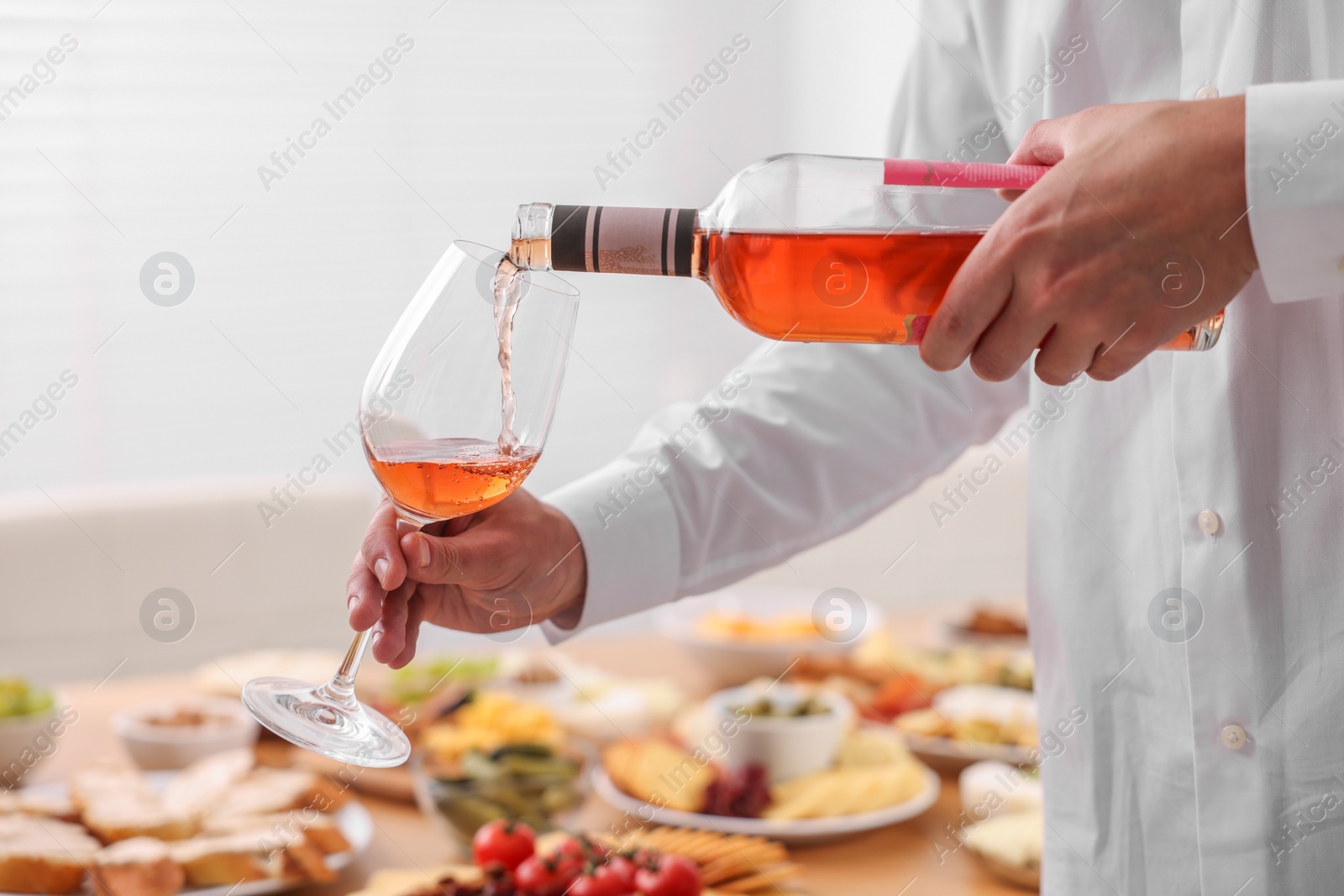 Photo of Man pouring rose wine from bottle into glass indoors, closeup