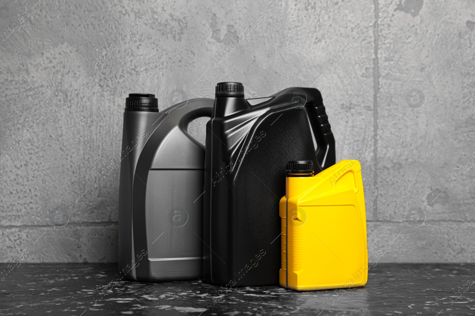 Photo of Motor oil in different canisters on black table near grey wall