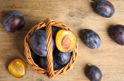 Delicious ripe plums in wicker basket on wooden table, flat lay