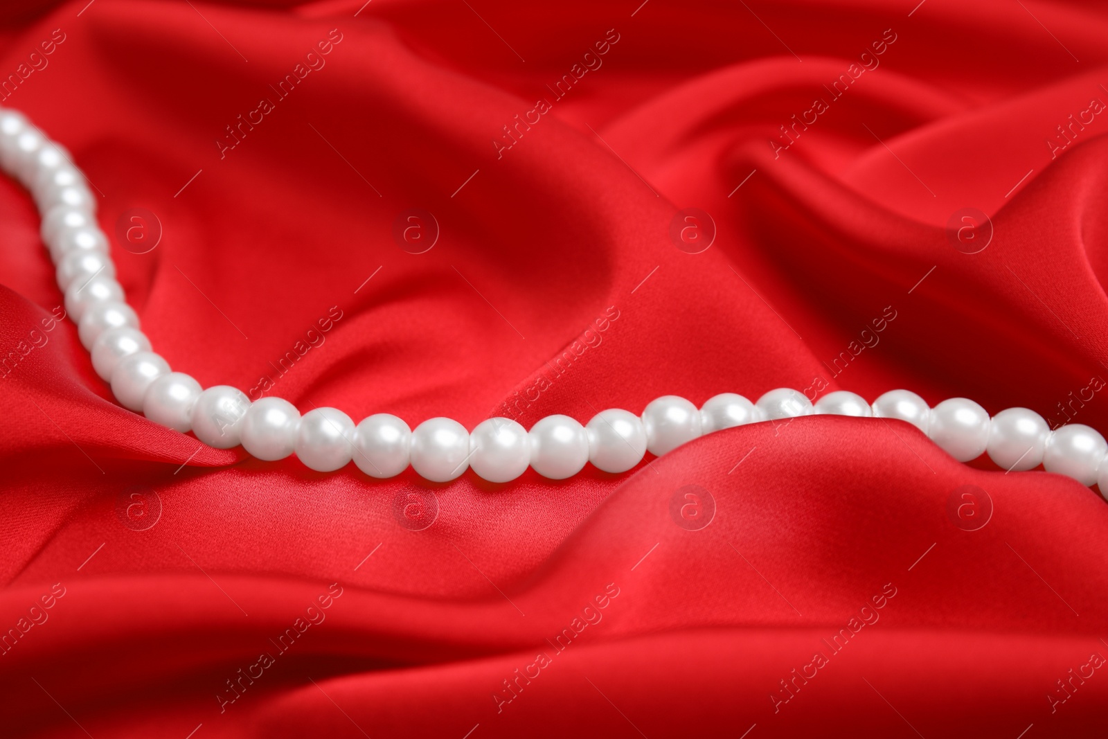 Photo of Beautiful white pearls on delicate red silk