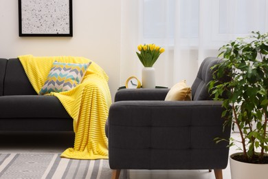 Photo of Spring atmosphere. Stylish living room interior with comfortable furniture and bouquet of beautiful yellow tulips