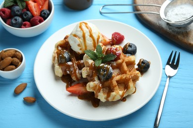 Photo of Delicious Belgian waffles with ice cream, berries and caramel sauce on light blue wooden table, closeup