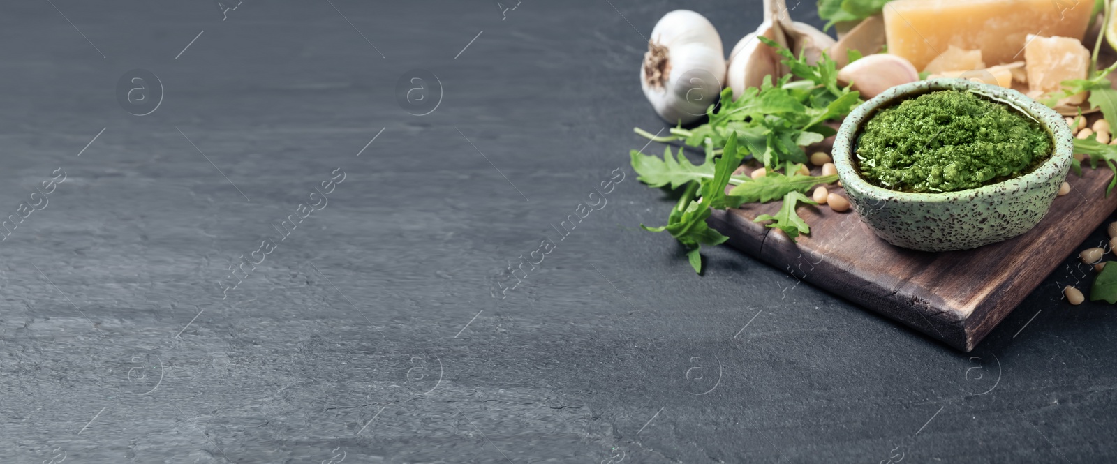 Image of Bowl of arugula pesto and ingredients on grey table, space for text. Banner design 