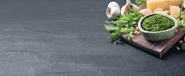 Bowl of arugula pesto and ingredients on grey table, space for text. Banner design 