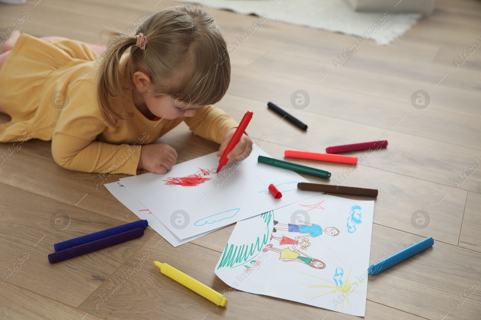 Photo of Cute little girl drawing with marker on floor indoors. Child`s art