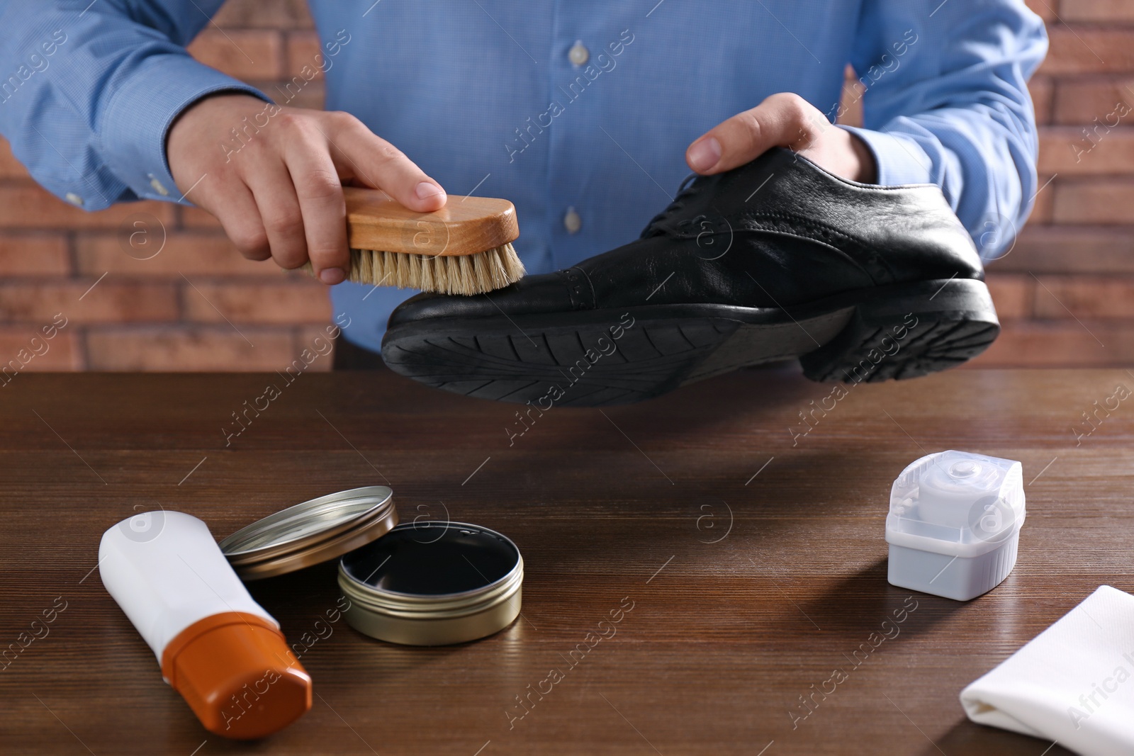 Photo of Man cleaning leather shoe at wooden table indoors, closeup