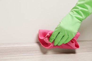 Photo of Woman in gloves cleaning plinth with cloth indoors, closeup. Space for text
