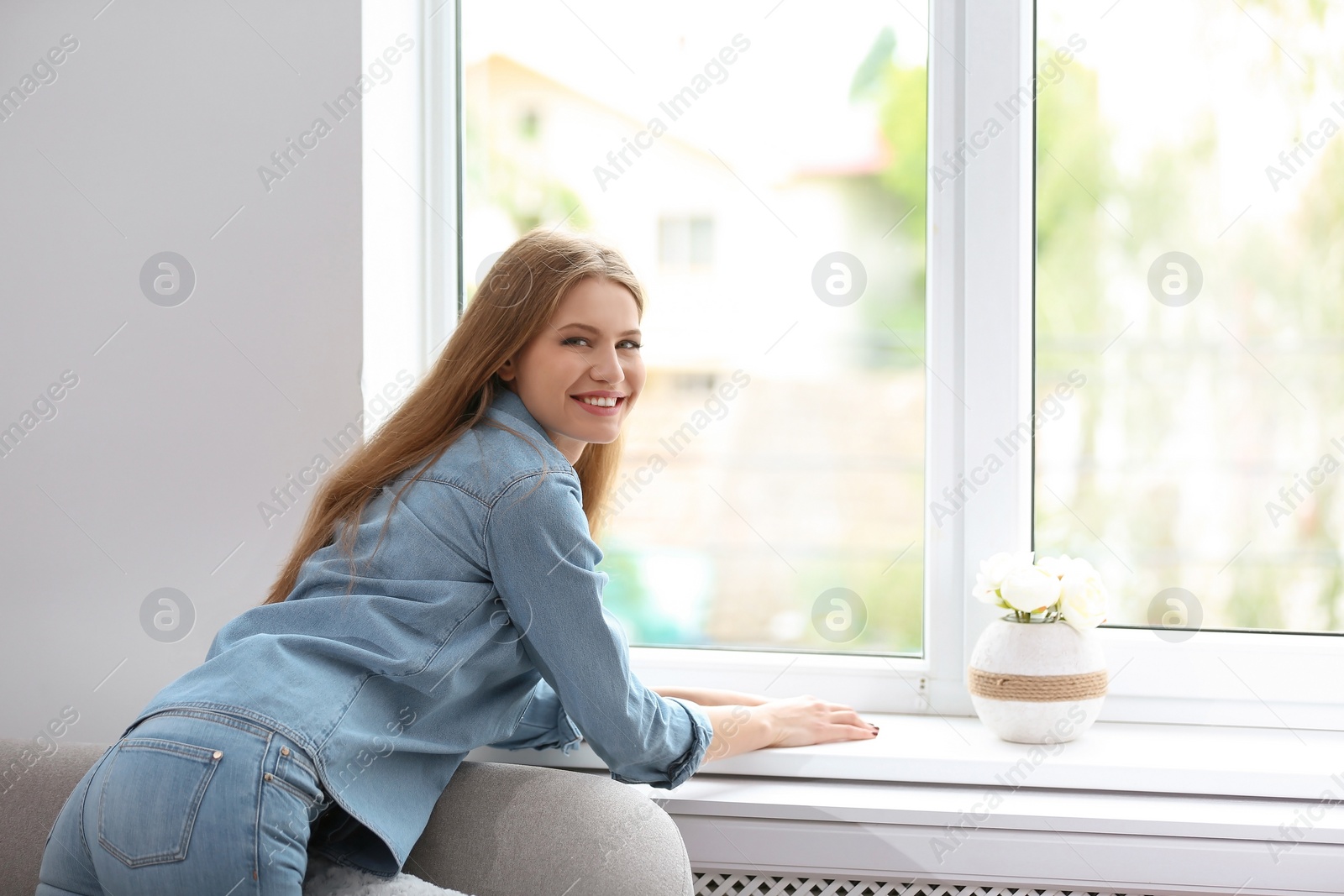 Photo of Young beautiful woman standing near window at home