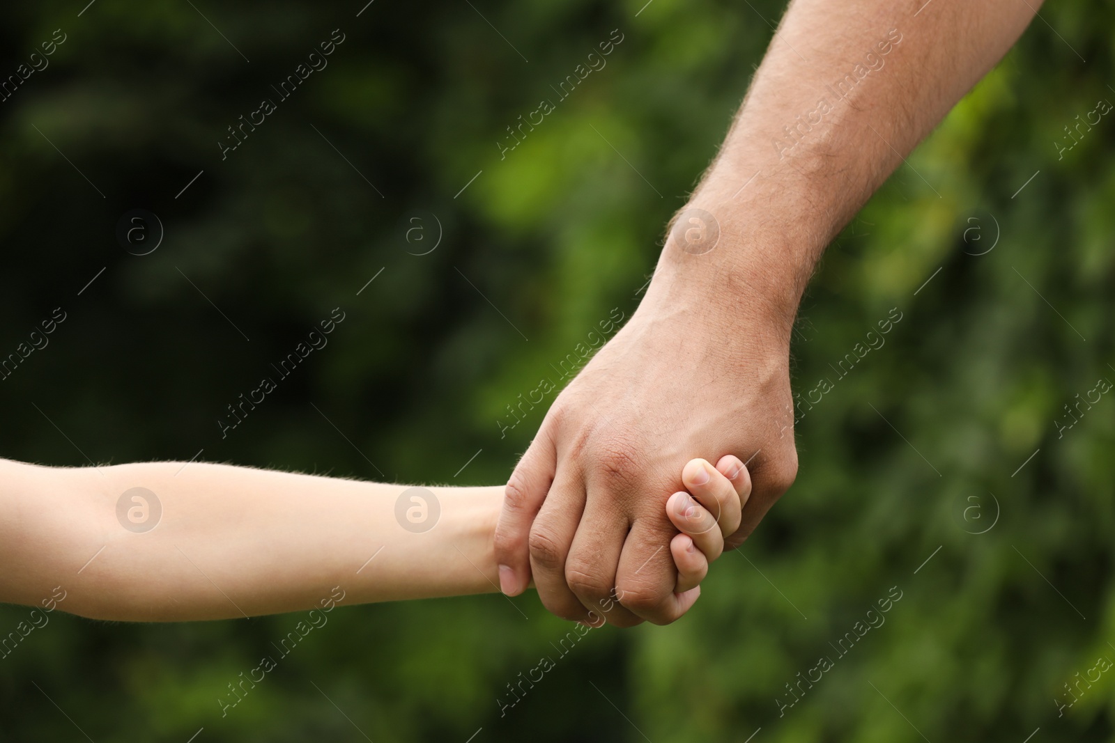 Photo of Man and child holding hands outdoors, closeup