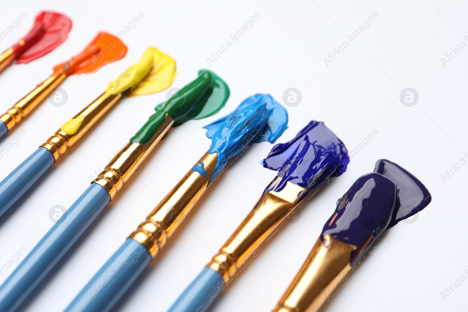 Photo of Set of brushes with different paints on white background, closeup. Rainbow colors