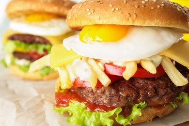 Photo of Tasty burgers with fried egg on parchment